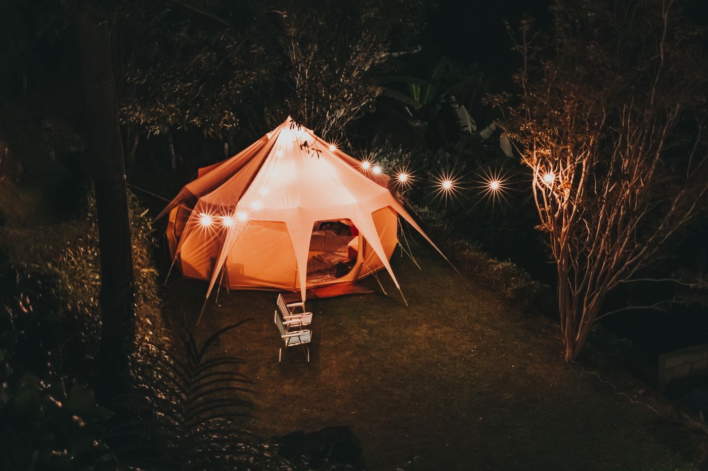 A canvas tent glowing at night with a string of warm lights strung beside it