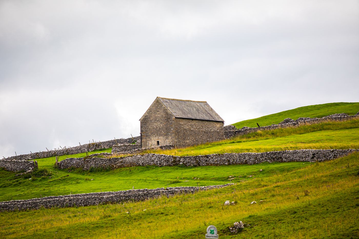 A traditional stone barn on a green hillside divided by dry-stone walls