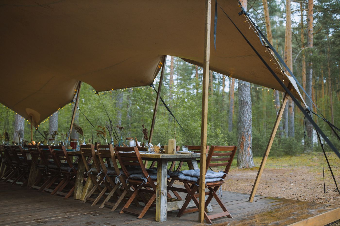A stretch tent open to the trees, with a long dining table set beneath it